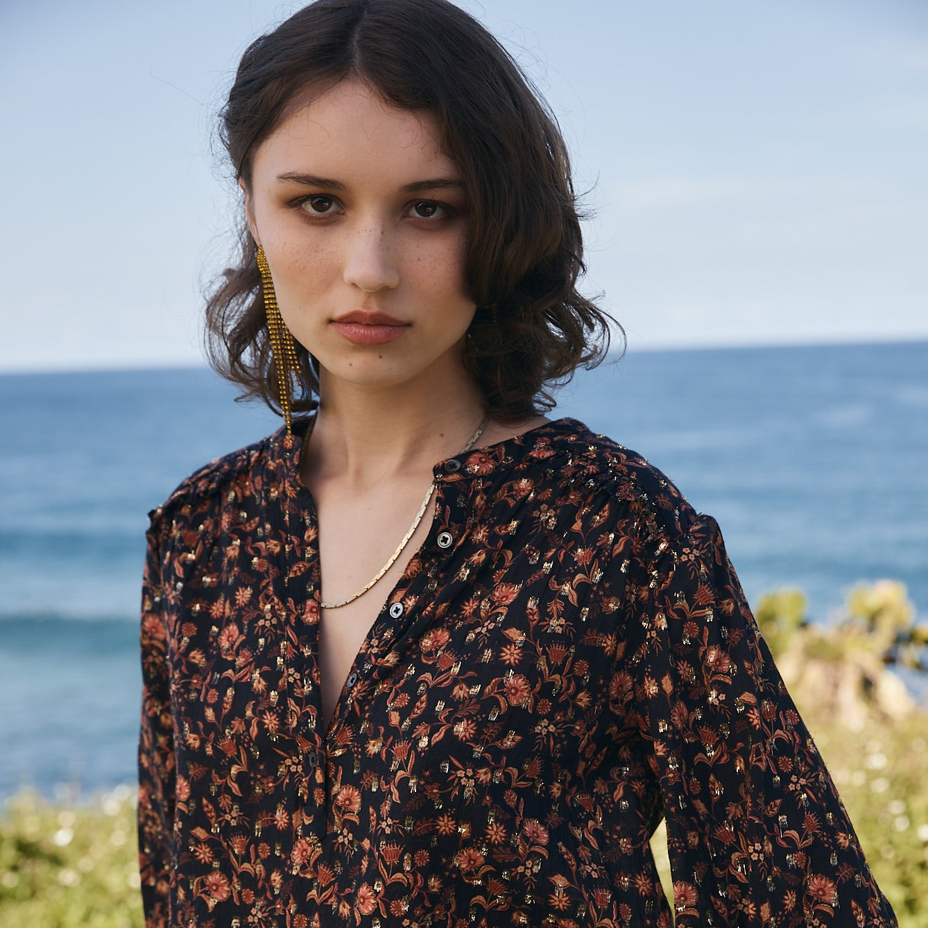 Woman wearing a floral blouse with a scenic ocean background
